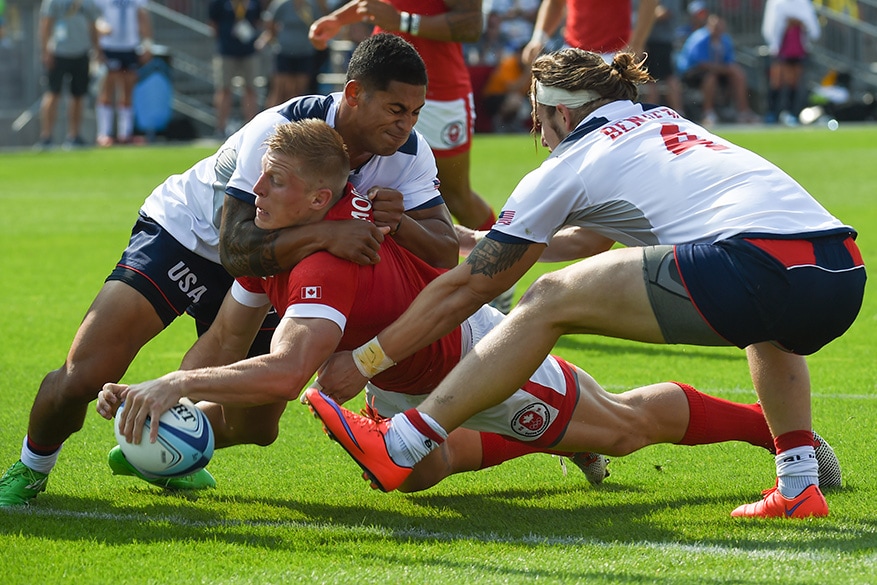 John Moonlight of Canada scores a tri despite the full effort of US defenders Garrett Bender and Nate Augspurger (4) in a men Rugby 7 semi-final match between Canada and the United States at Exhibition Stadium on Sunday. Canada won 26-19.