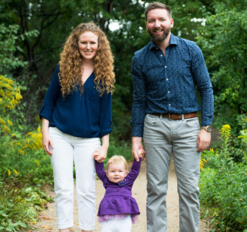 Parents holding their baby's hand in a park as they pose for a family photo