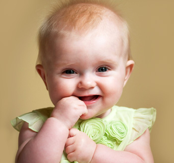 Photo of an adorable small baby wearing a dress and sucking her finger