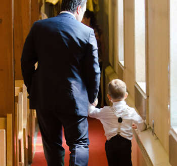 Father holds his son's hand and walks down church isle during a baptism ceremony