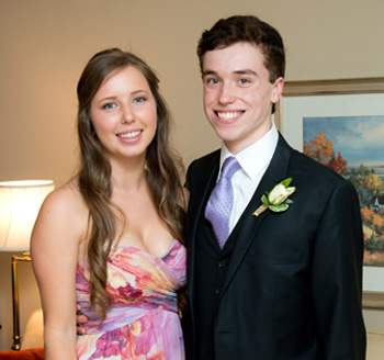 Two young teenagers dressed elegantly pose side-by-side for their prom photo