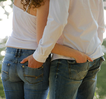 Young engaged couple pose with hands in each other's pockets during an engagement photo