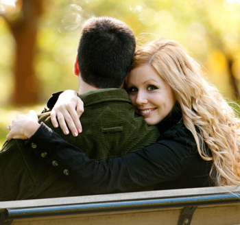 Newly engaged couple pose on a park bench for a fall engagement photo