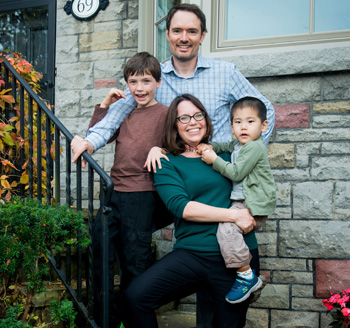 Mother and father standing on their home's front steps and posing with their two children