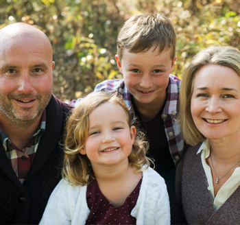 Parents and two young children pose with big smiles for a beautiful family photo