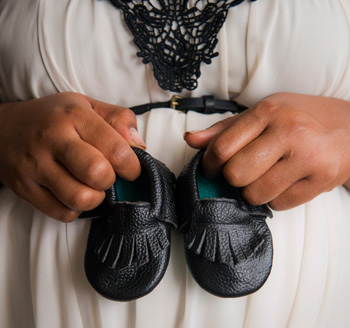 Mother-to-be holds her newborn baby's boots in front of her belly