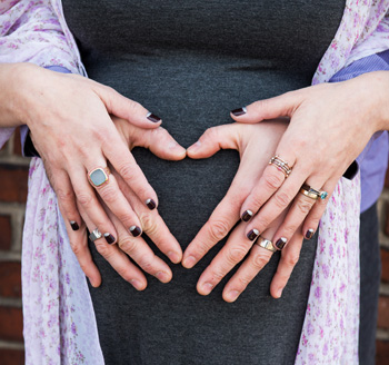 Husband and wife place their hands over her pregnant belly in a loving photo
