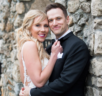 Young couple pose against a brick wall for their wedding photo