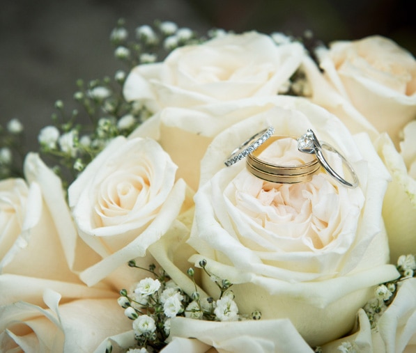 Wedding rings sit on top of a beige wedding bouquet
