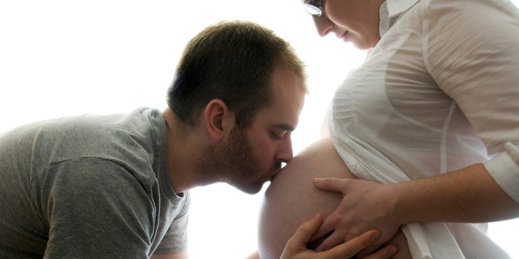 Pregnant woman holding her belly while her husband kisses her gently